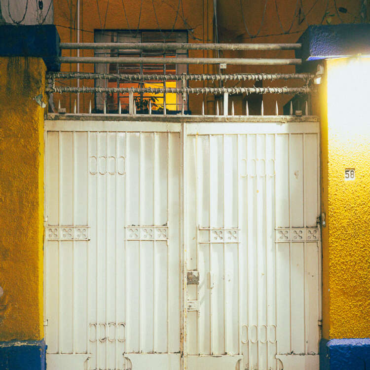 Oaxaca street photography print featuring warm yellow walls, a white gate, tangled wires, and cinematic evening light.