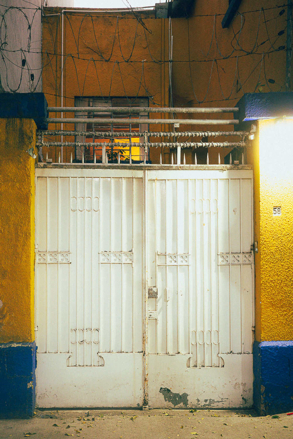 Oaxaca street photography print featuring warm yellow walls, a white gate, tangled wires, and cinematic evening light.